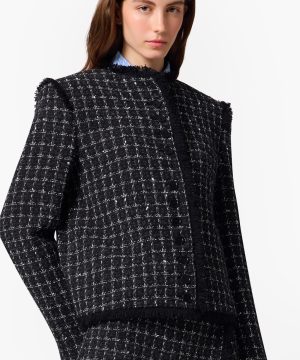 Model wearing a black tweed check jacket with fringe trim and a row of black buttons.