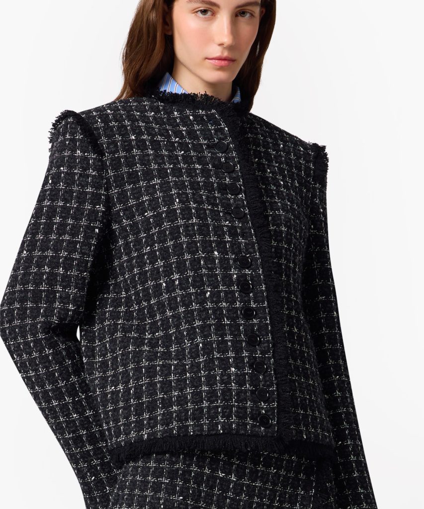 Model wearing a black tweed check jacket with fringe trim and a row of black buttons.