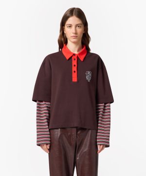Model wearing a dark brown polo with a bright red collar and placket, striped long-sleeve layer underneath, and brown leather pants.