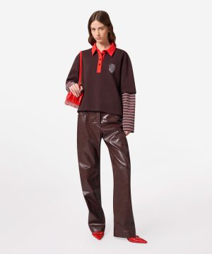 Fashion model wearing a burgundy polo with a red collar and placket, striped long sleeves, shiny brown leather pants, and red handbag and shoes.