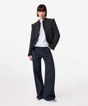 Fashion model wearing a black-and-white textured tweed jacket, white top, and navy wide-leg pants, posing confidently.