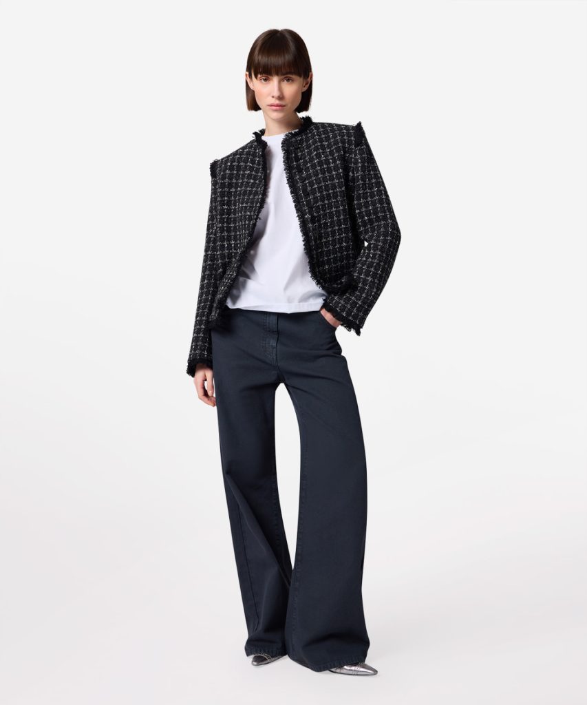 Fashion model wearing a black-and-white textured tweed jacket, white top, and navy wide-leg pants, posing confidently.