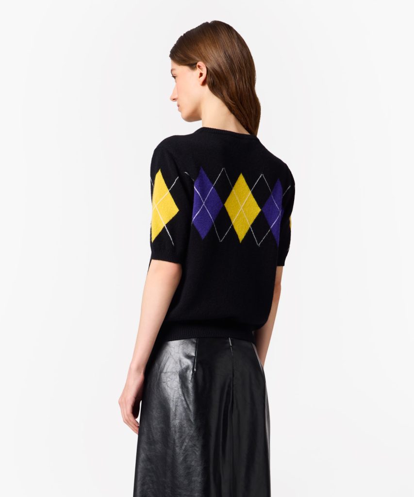 Back view of a black knit sweater with a yellow and purple argyle diamond pattern, worn by a model