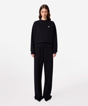 Model wearing an oversized black sweatshirt with a small logo, paired with wide-leg black trousers.