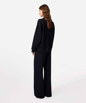 Person wearing a black oversized sweatshirt and wide-leg pants, seen from the back.