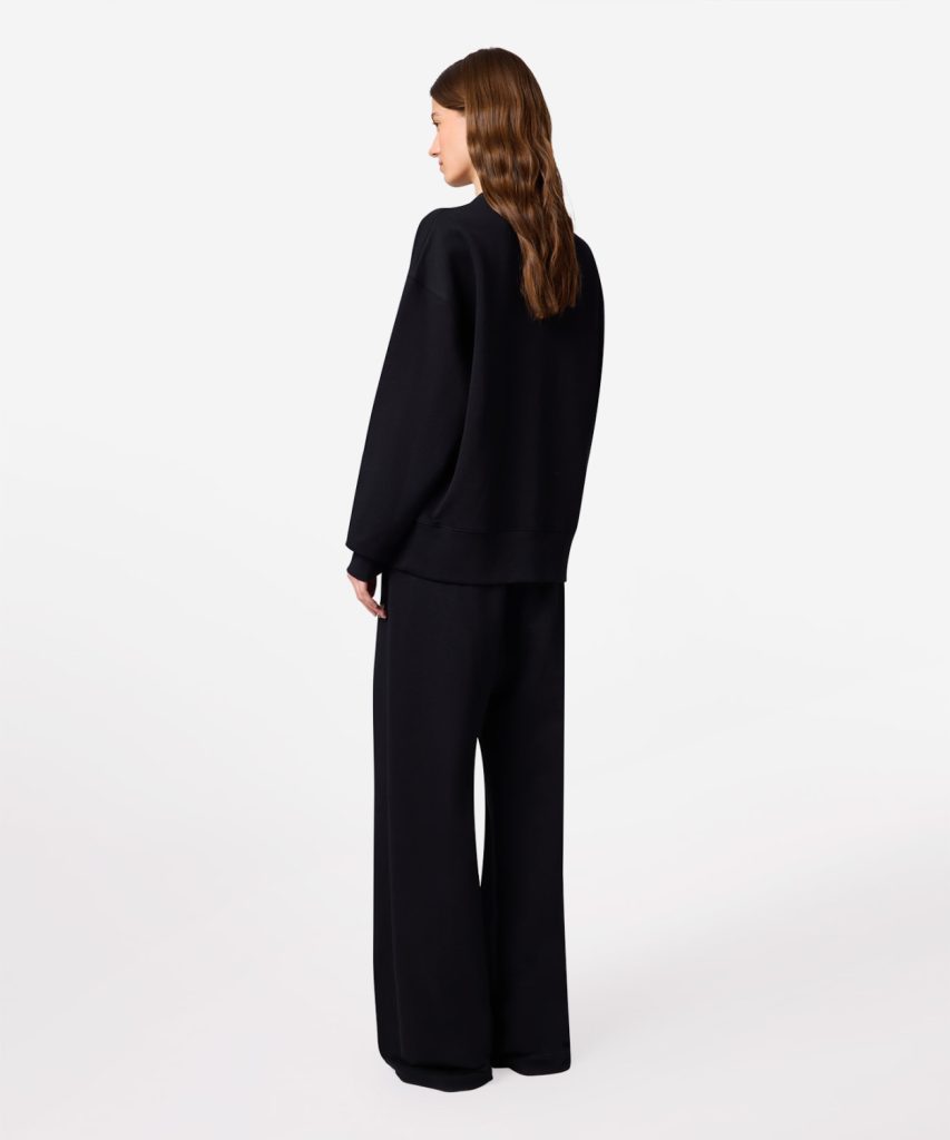 Person wearing a black oversized sweatshirt and wide-leg pants, seen from the back.