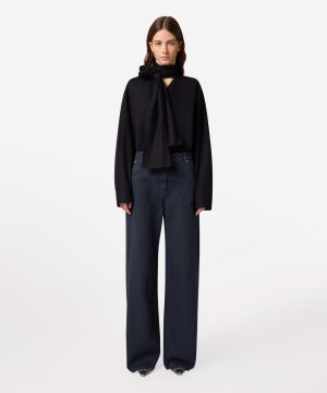 Model wearing a black blouse with a neck bow and wide-leg dark jeans against a white background.