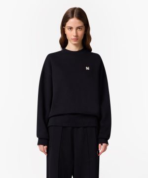 Woman in a black sweatshirt with a small embroidered N on the left chest, against a white backdrop.