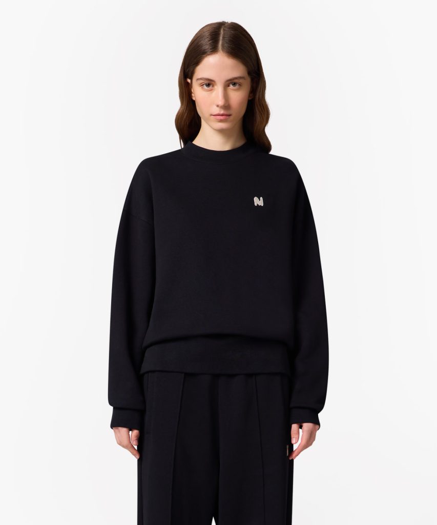 Woman in a black sweatshirt with a small embroidered N on the left chest, against a white backdrop.