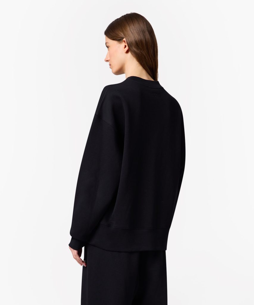 Back view of a person wearing an oversized black sweatshirt against a white background.
