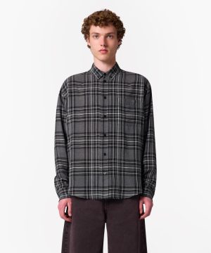 Model wearing a gray plaid button-up shirt with long sleeves and dark pants, standing against a white background.