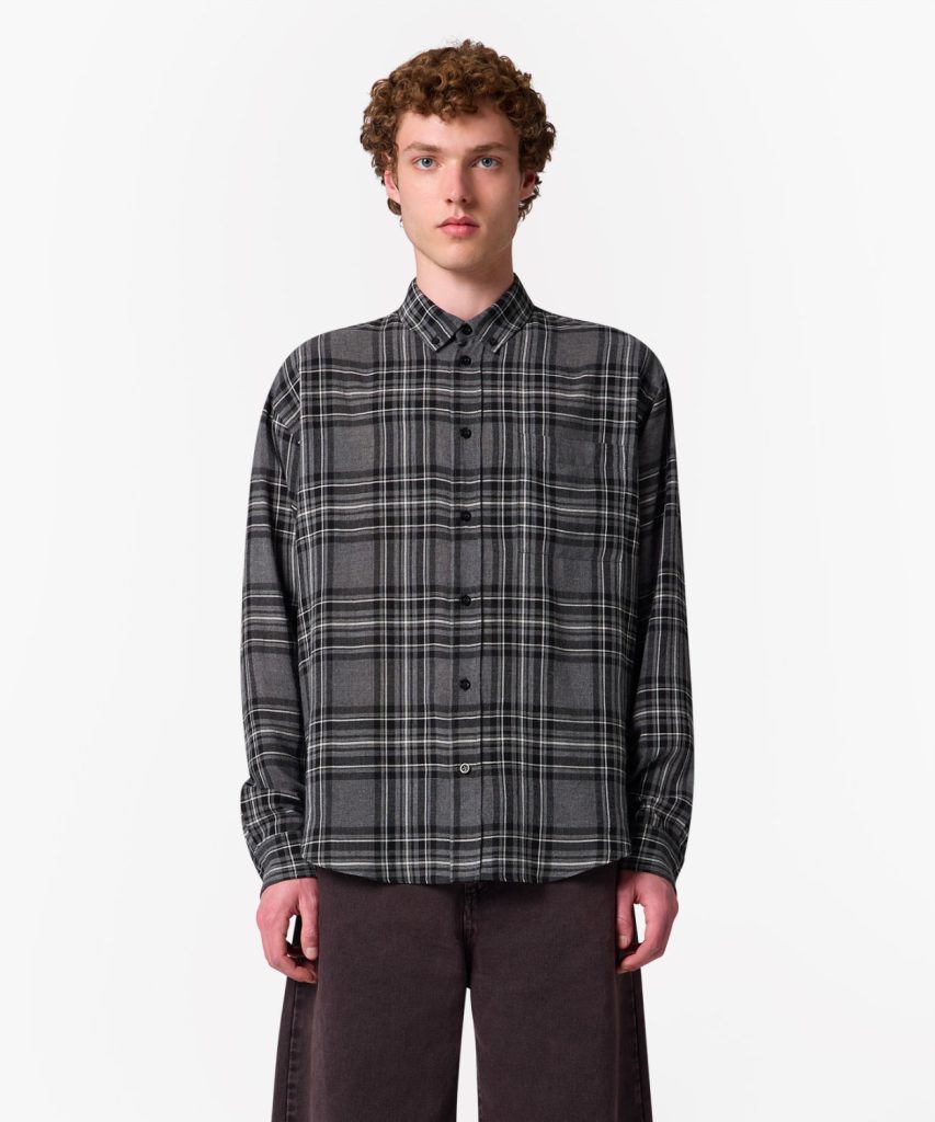 Model wearing a gray plaid button-up shirt with long sleeves and dark pants, standing against a white background.