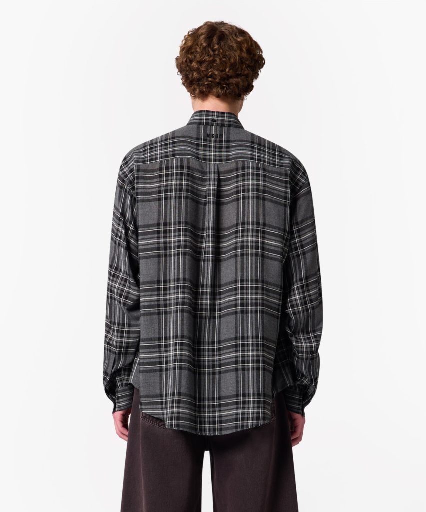 Back view of a person wearing a gray plaid flannel shirt, standing against a white background.