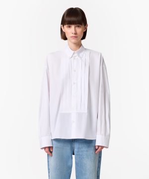 Woman wearing a crisp white button-down shirt with pleated front panels, paired with light blue jeans, facing the camera.