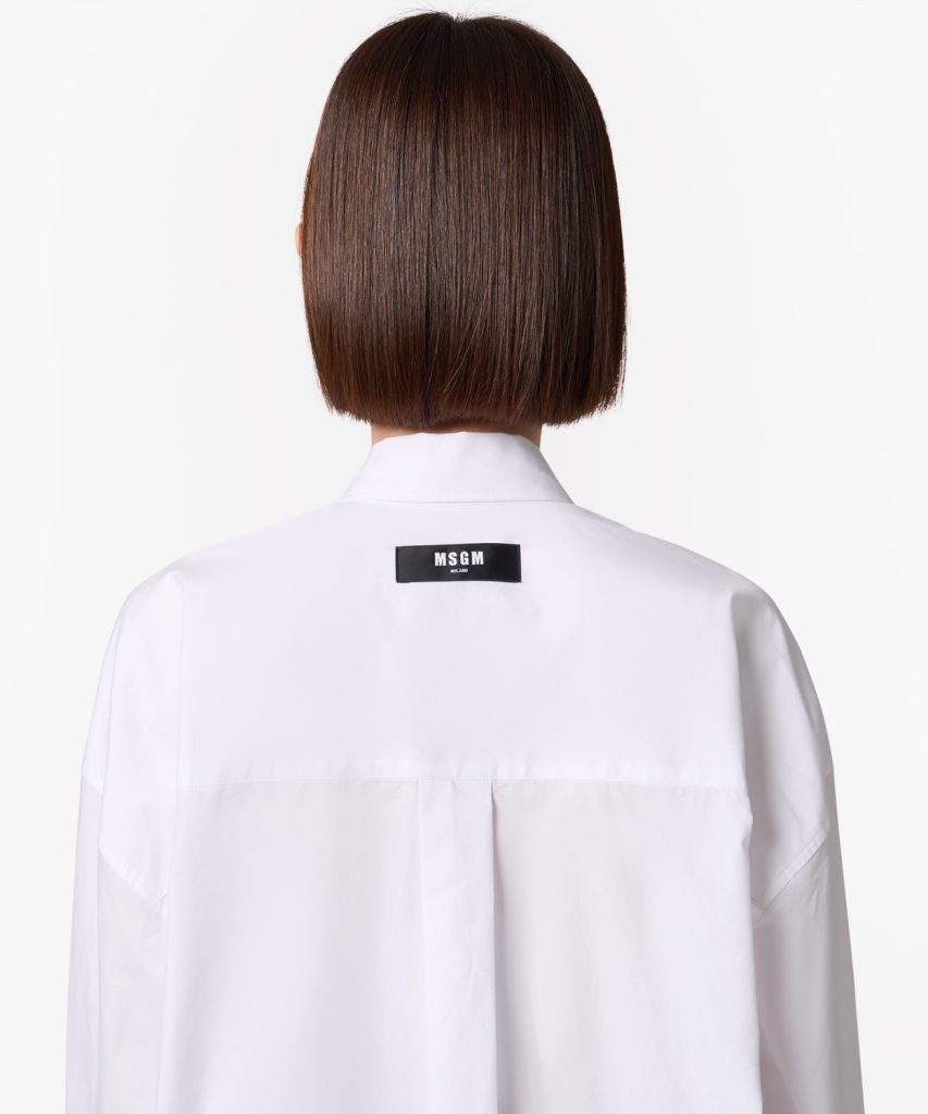 Back view of a person with a sleek brown bob hairstyle wearing a white coat with an MSGM Milano label on the upper back