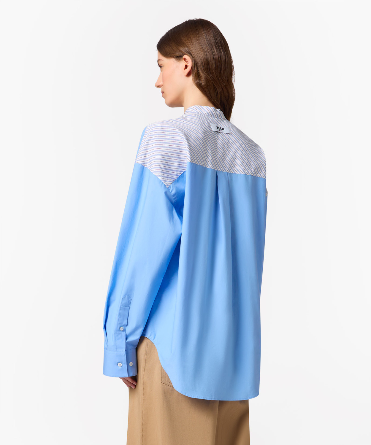IMG_3242 - New Trend Back view of a person wearing a light blue oversized shirt with a striped yoke and tan pants, standing against a white background