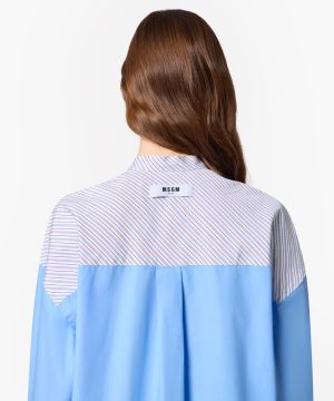 Back view of a person wearing a light blue shirt with a striped yoke; a white MSGM label sits at the upper back collar.