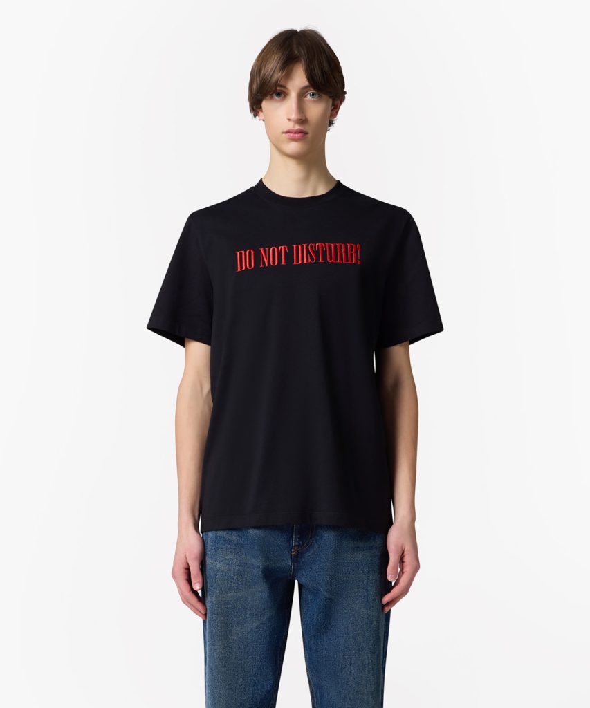 Person wearing a black T-shirt with red 'DO NOT DISTURB!' text across the chest, model standing against a light background