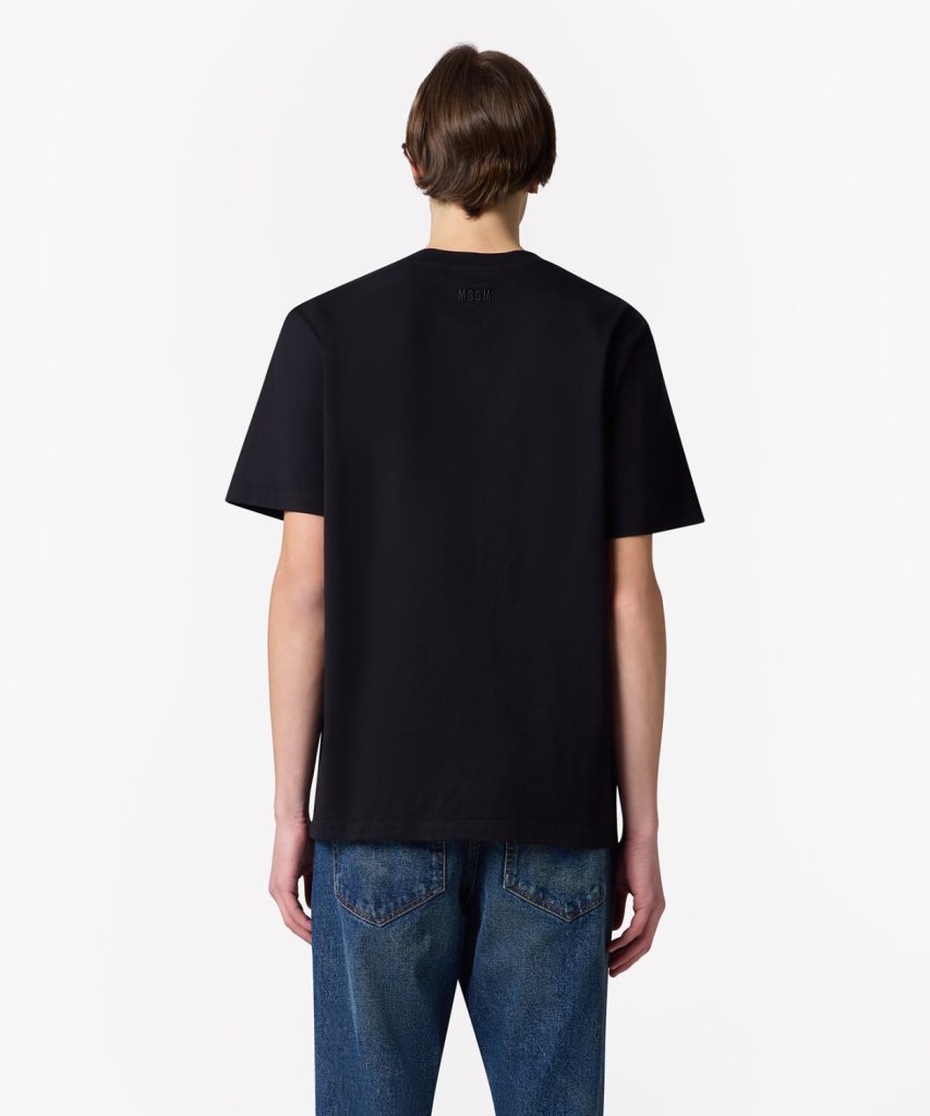 Back view of a person wearing a black short-sleeve tee and blue jeans; small MSGM logo on upper back.
