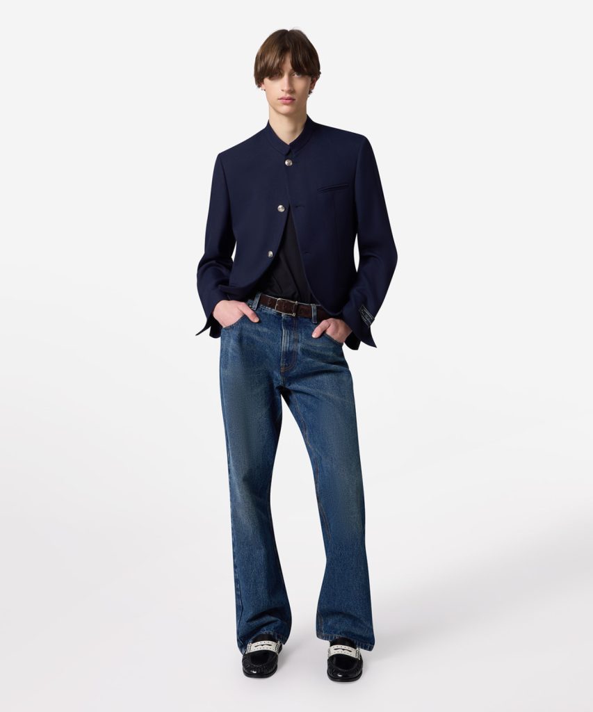 Person wearing a navy cropped blazer with a black top and wide-leg jeans, hands in pockets, standing against a light background
