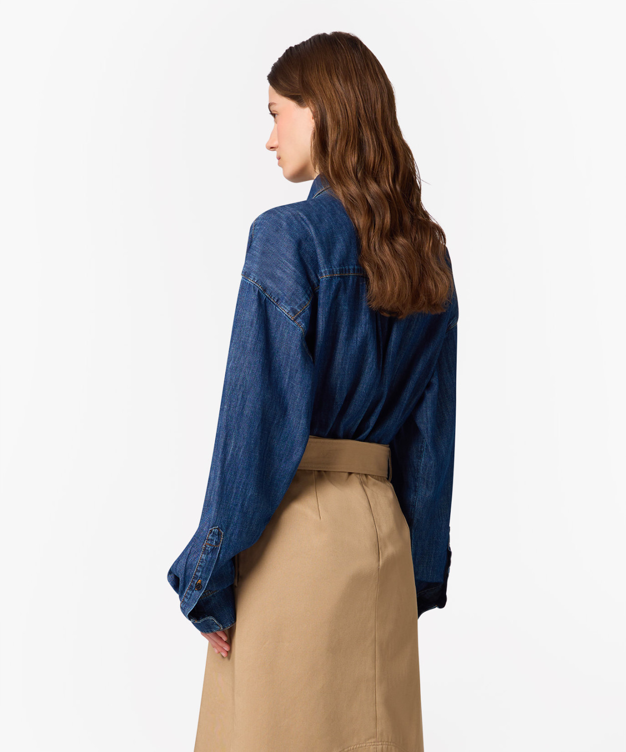 IMG_3257 - New Trend Back view of a person in a blue denim shirt tucked into a tan skirt, with long wavy brown hair.