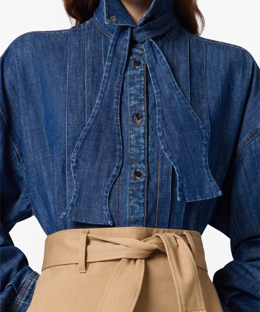 Close-up of a person wearing a dark blue denim shirt with a tied neck scarf and a tan high-waisted belt at the waist.