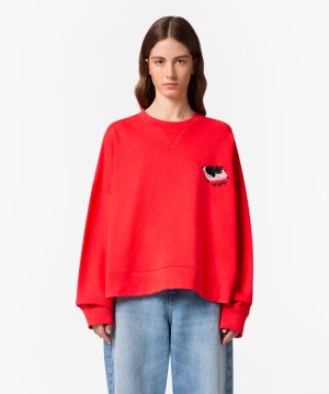 Young woman wearing a bright red oversized sweatshirt with a small black cat graphic on the left chest, against a white background.