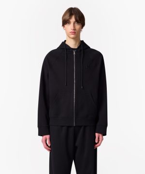 Person wearing a black zip-up hoodie with drawstrings and front pockets, standing against a white background.