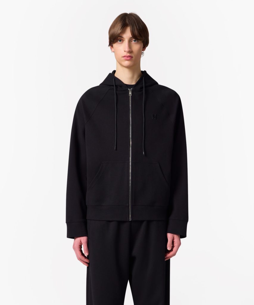 Person wearing a black zip-up hoodie with drawstrings and front pockets, standing against a white background.