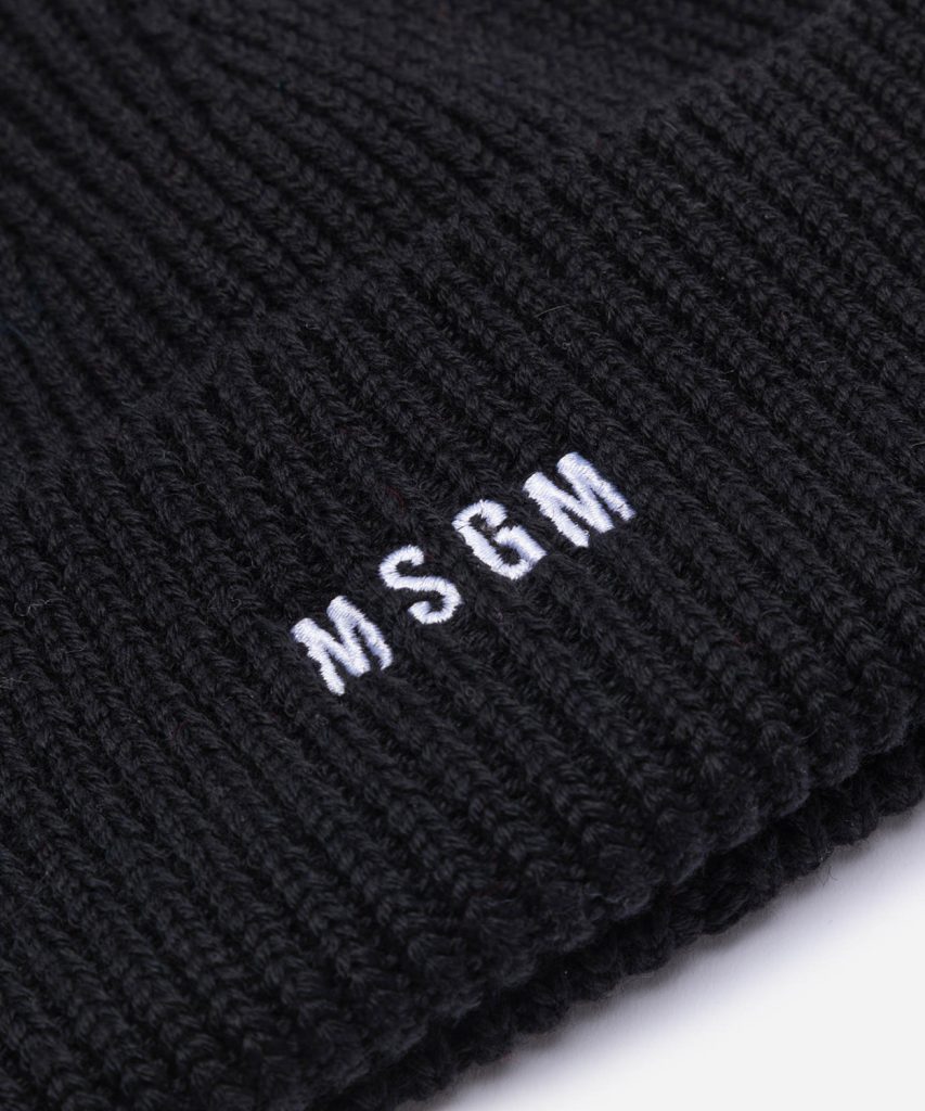 Close-up of a black knit fabric with white embroidered letters reading WSCM.