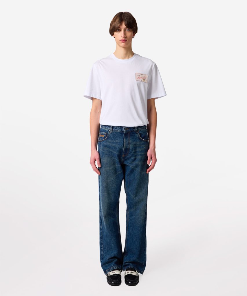 Model wearing a white short-sleeve T-shirt with loose blue jeans, standing against a plain light background.
