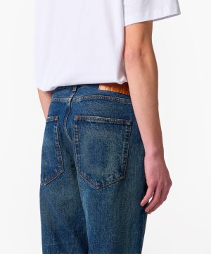 Back view of a person wearing a white t-shirt tucked into blue denim jeans with a brown leather brand tag at the waistband.