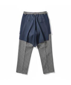 Layered navy shorts over checkered gray pants on a white background, fashion look.