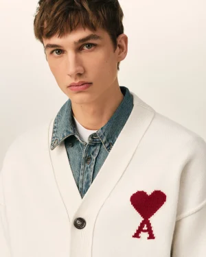 Close-up of a person wearing a white cardigan with a red knitted heart patch over a denim shirt.