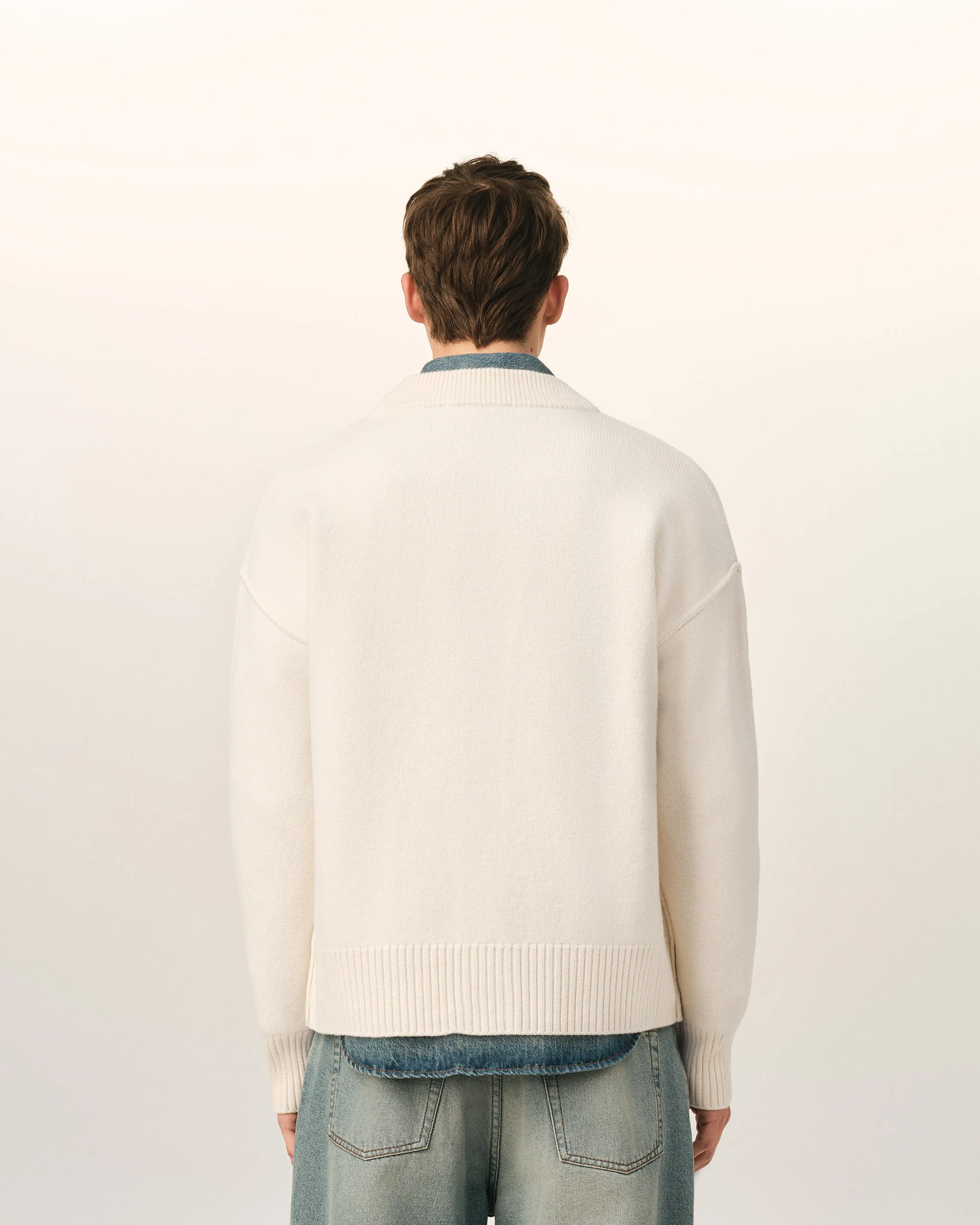 IMG_3436 - New Trend Back view of a person wearing a cream knit sweater and blue jeans against a pale background.