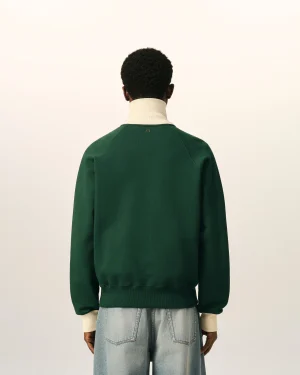Back view of a person wearing a dark green sweater over a cream turtleneck, with light-wash jeans, standing against a neutral background.