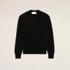 IMG_3454 - New Trend Flat lay of a black knit crewneck sweater on a pale beige background, label visible at the neckline, minimal styling.