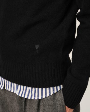 Close-up of a black knit sweater over a blue-and-white striped shirt, with a small heart-shaped patch visible on the sweater.