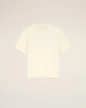 Cream short-sleeve T-shirt laid flat on a pale background with a small heart emblem on the chest and a visible tag at the neckline.