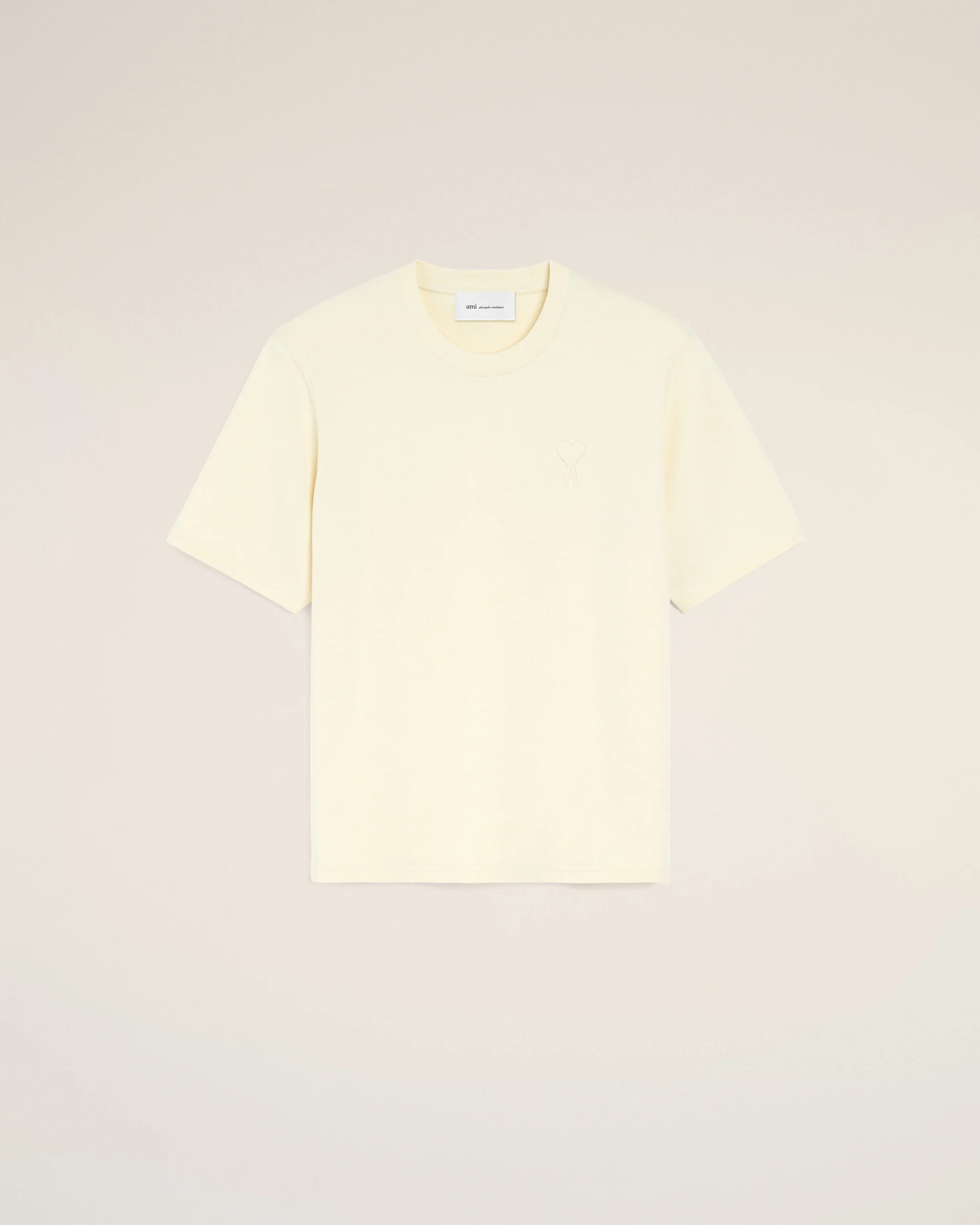 IMG_3459 - New Trend Cream short-sleeve T-shirt laid flat on a pale background with a small heart emblem on the chest and a visible tag at the neckline.