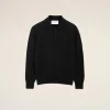 Black polo sweater with collar and button placket, shown from the chest up against a beige background, small left-chest logo visible.