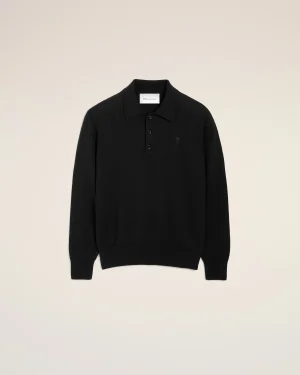 Black polo sweater with collar and button placket, shown from the chest up against a beige background, small left-chest logo visible.