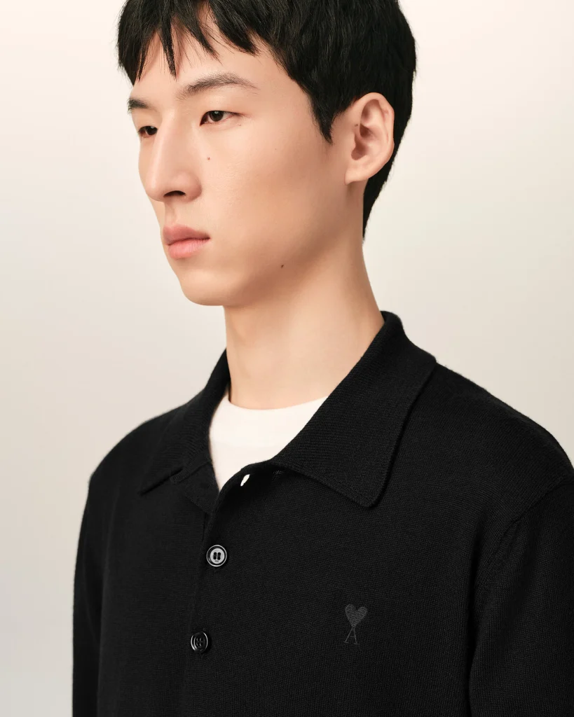 Close-up side profile of a young man wearing a black cardigan with a small heart embroidery on the chest.