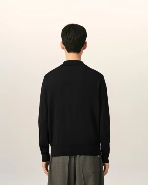 Back view of a person wearing a black sweater and gray pants against a light neutral background.