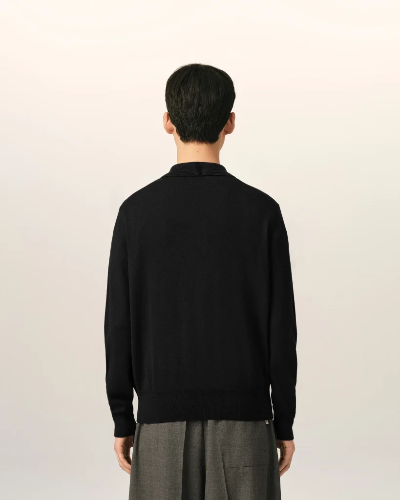 Back view of a person wearing a black sweater and gray pants against a light neutral background.