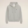 Light gray zip-up hoodie with drawstrings and a small black heart emblem on the left chest against a beige background.