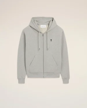 Light gray zip-up hoodie with drawstrings and a small black heart emblem on the left chest against a beige background.