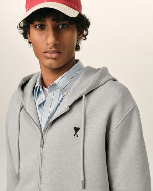 Close-up of a person wearing a gray zip hoodie over a blue striped shirt and a red cap; neutral background (fashion photo)