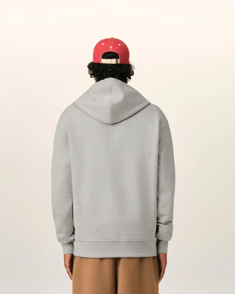 Person facing away from the camera, wearing a light gray hoodie and a red baseball cap, with brown pants visible at the bottom edge.