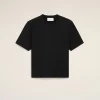 Flat-lay of a black short-sleeve t-shirt on a beige background; small stitched heart logo on the chest and a white neck tag visible.